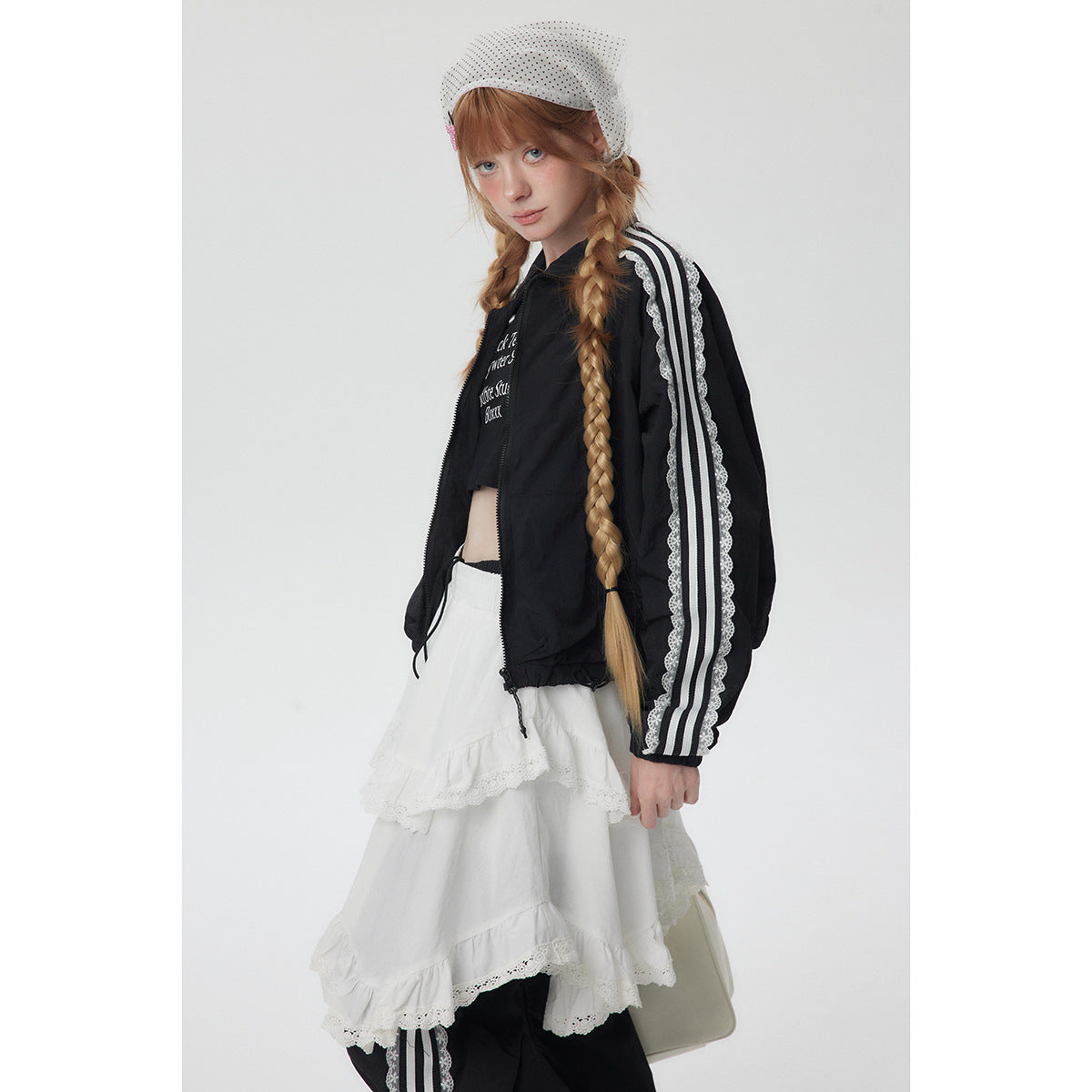 Side-angle view of a model in a black jacket with white striped lace-trim sleeves and a white tiered lace skirt.
