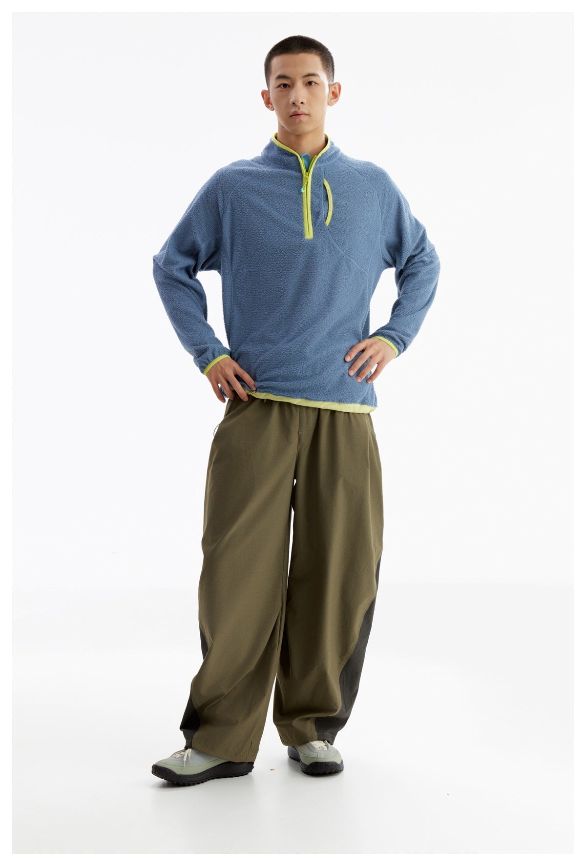 Front view of a model in a blue fleece pullover with lime trim and loose olive pants.