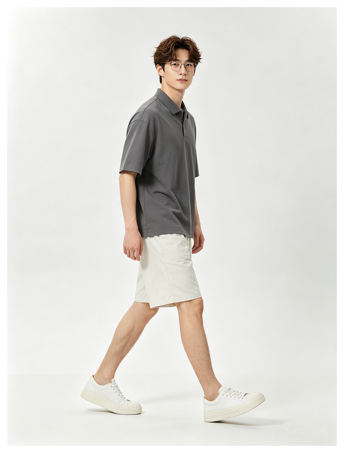 Model wearing a charcoal short-sleeve polo, white shorts and white sneakers, shown against a plain studio background.