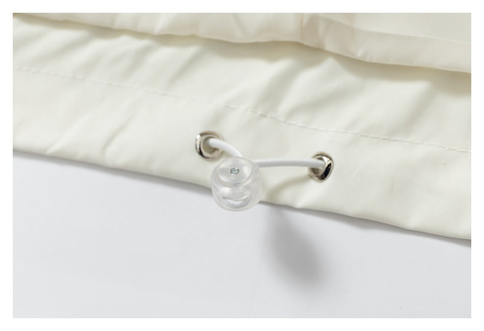 Close-up of a cream garment hem with metal eyelets and an adjustable drawcord toggle.