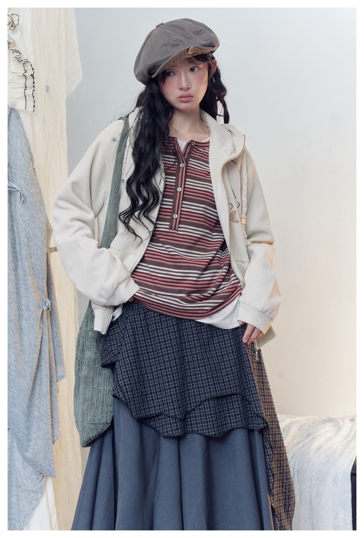 Model wearing an open ivory celestial-print hoodie over a burgundy striped top and layered dark skirt.