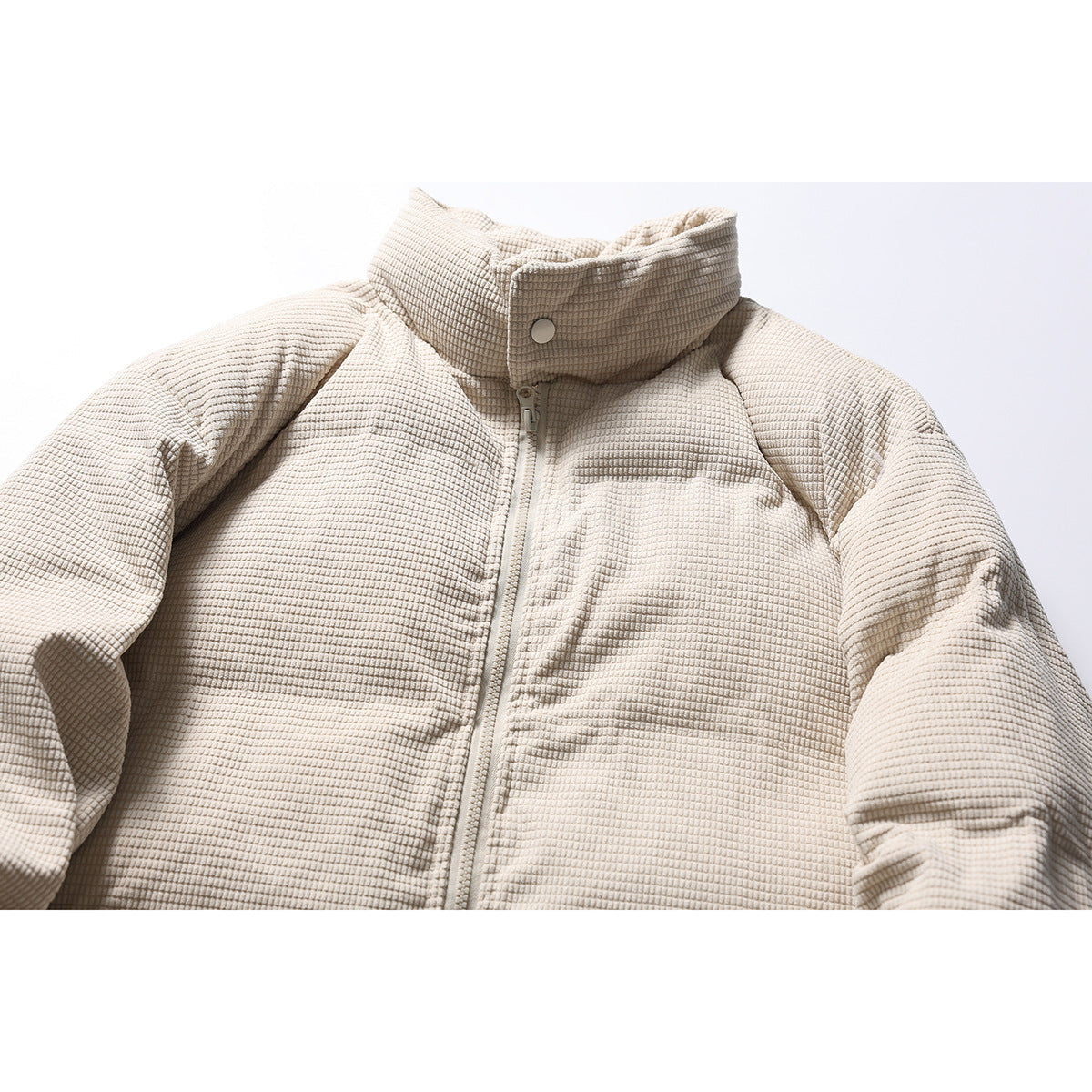Close-up of a cream textured padded jacket front, showing its high snap collar and central zipper.