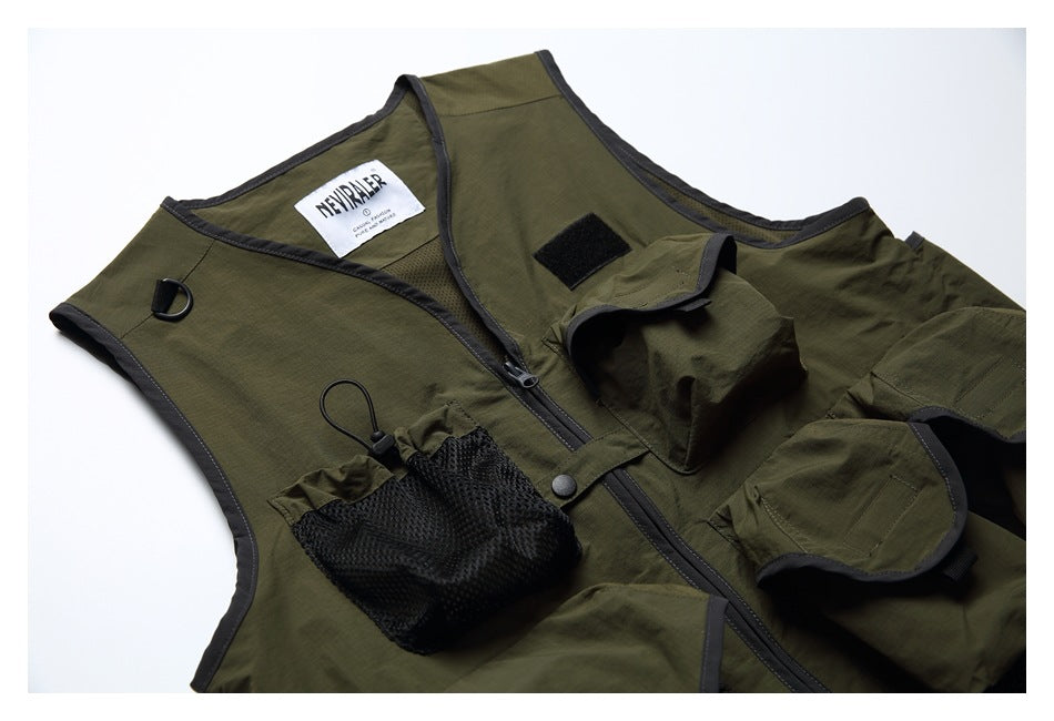 Close view of an olive utility vest with dark trim, zipper, mesh and flap pockets, a D-ring and hook-and-loop patches.
