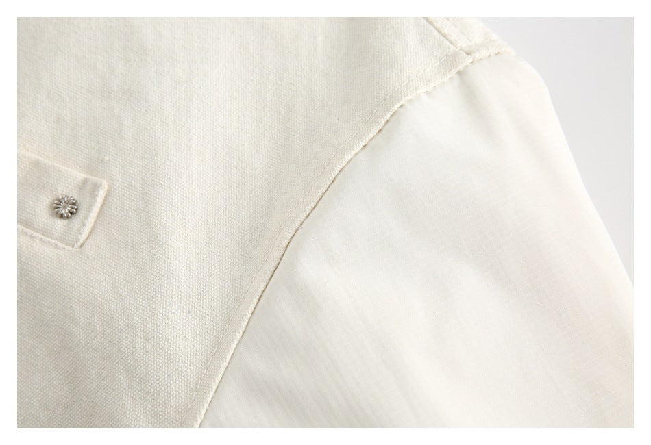 Close-up of a cream garment's shoulder seam and smooth sleeve, with part of a snap-tab pocket visible.