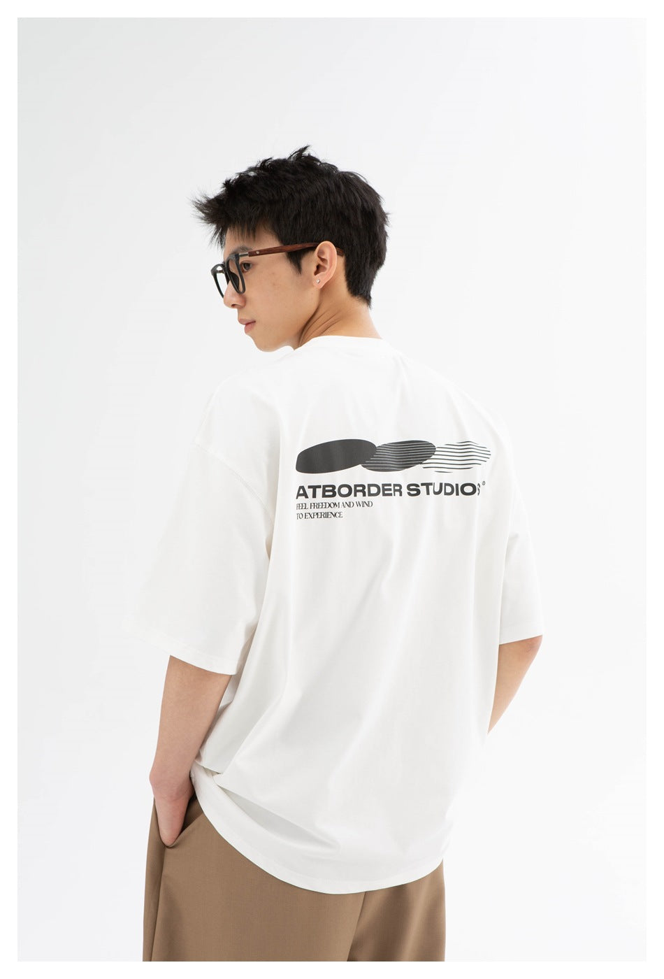 Model shown from behind in a white oversized T-shirt with a large black back graphic and English lettering.
