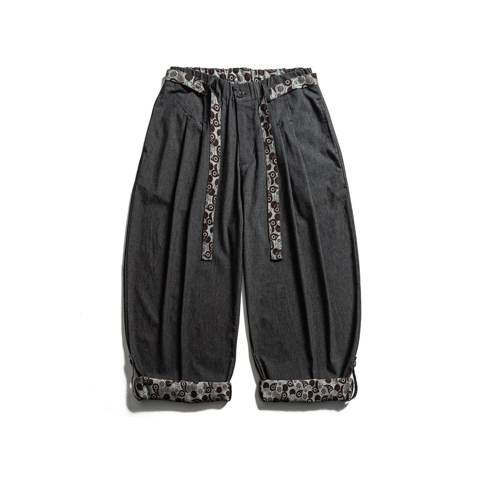 Front view of loose charcoal trousers with a patterned waistband, long matching straps and turned-up patterned cuffs.