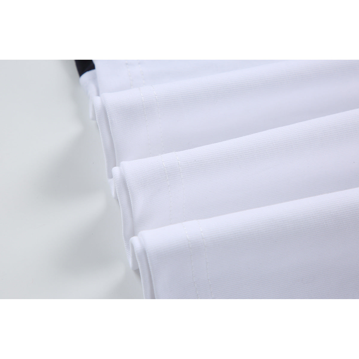 Close-up of several white shirt hems showing folded edges and parallel stitching.