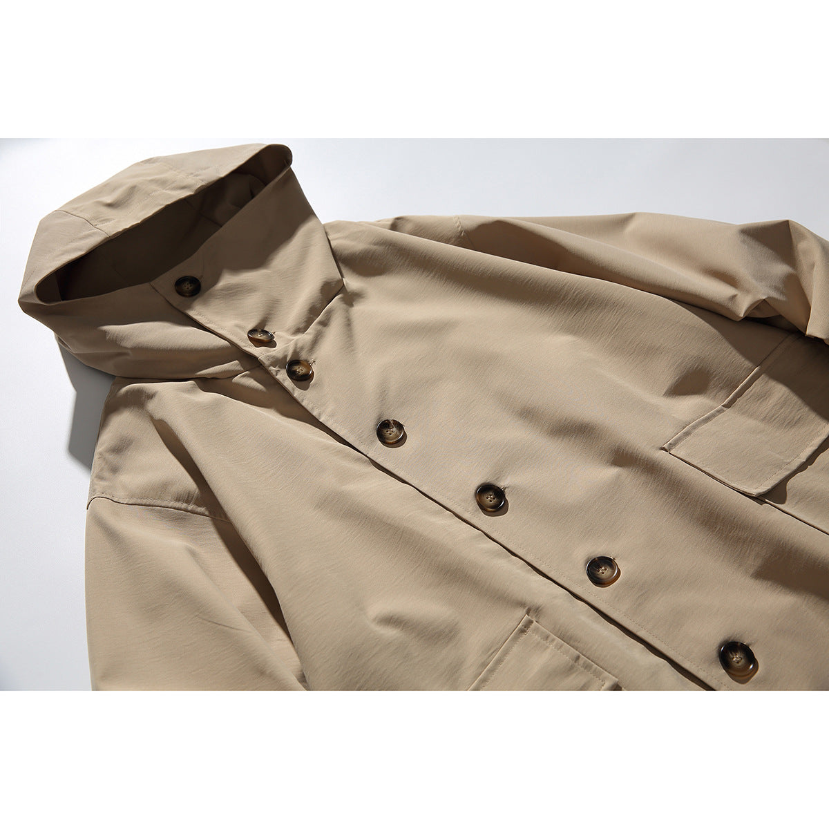 Close-up of a tan hooded coat showing the high collar, dark buttons and part of a front pocket.