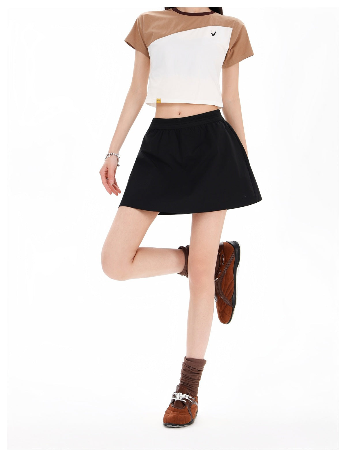 Front view of a model wearing a brown-and-white color-block cropped T-shirt with a black flared mini skirt.