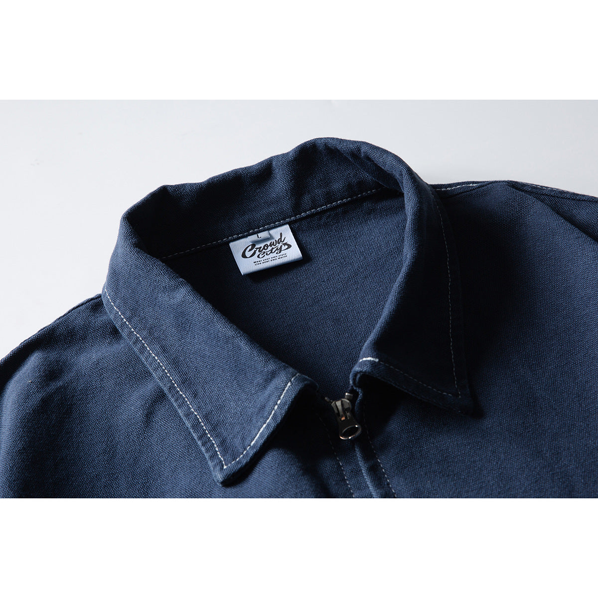 Close-up of a navy jacket's pointed collar, zipper, contrast stitching, and sewn neck label.