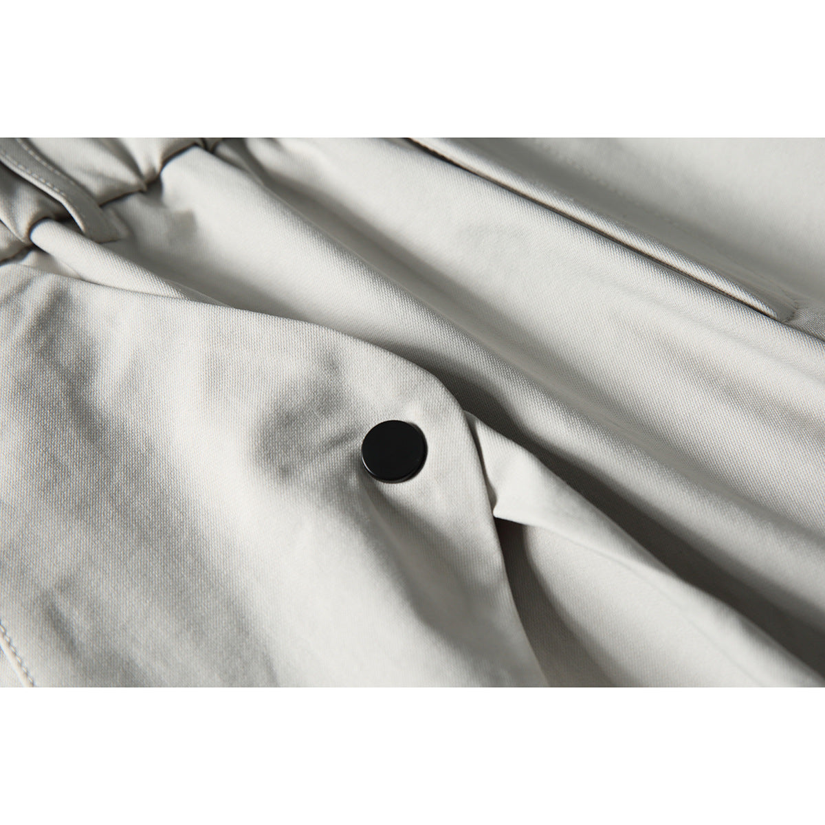 Close-up of light gray trousers showing a black button and stitched fabric folds.