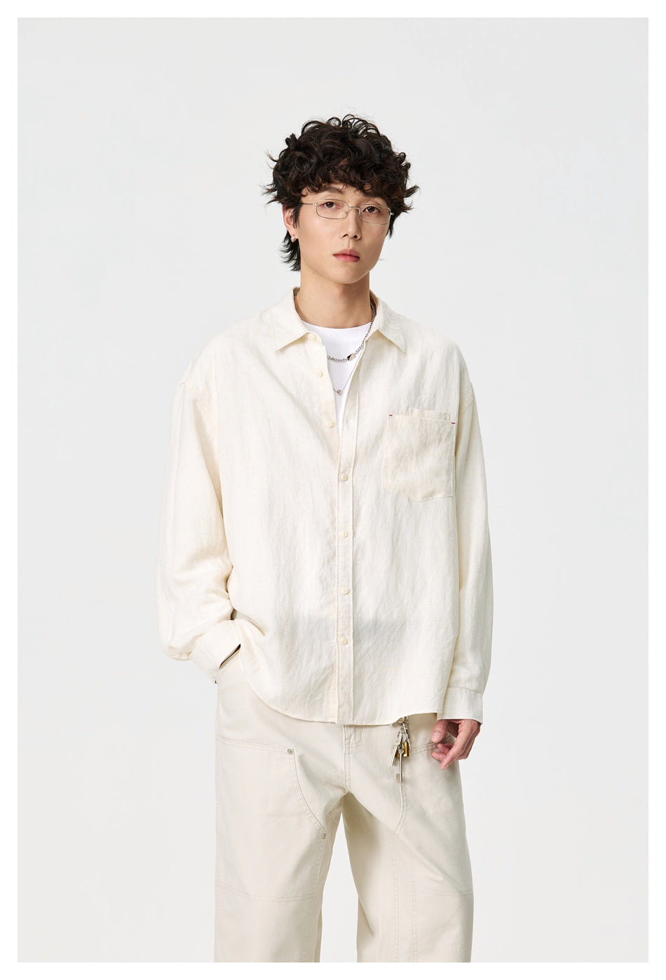 Front view of a model wearing a relaxed ivory button-up shirt with a chest pocket and cream trousers.
