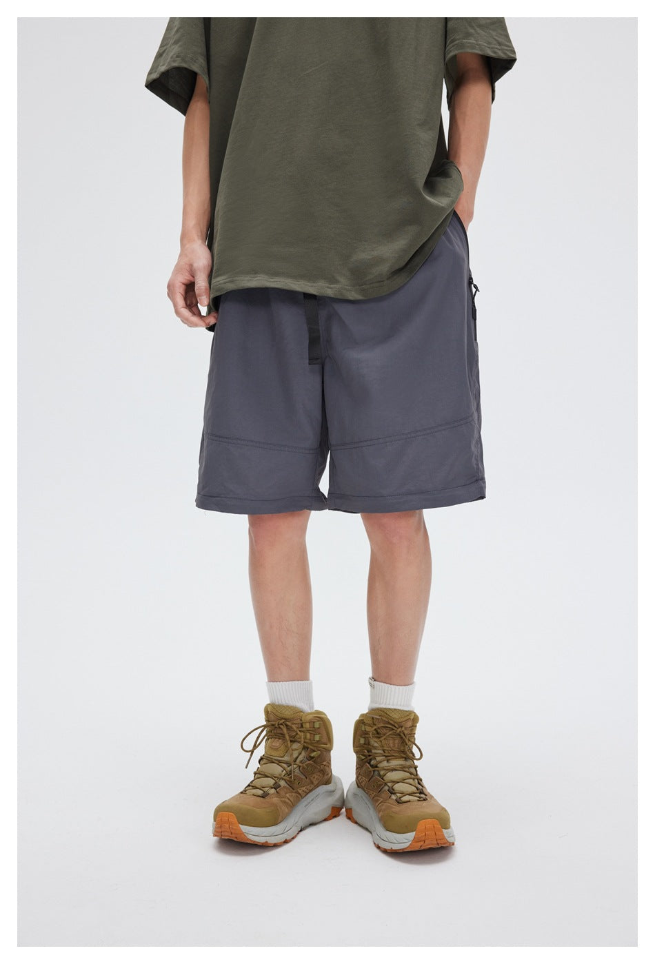 Front view of a model wearing loose slate-gray shorts with a black drawstring and zip pockets.