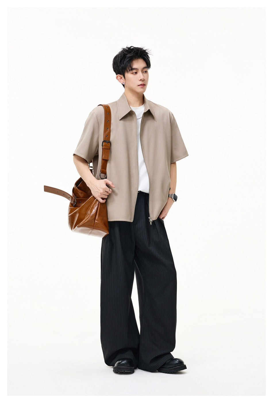 Full-length view of a model wearing a taupe short-sleeve collared zip-front shirt with wide black trousers.