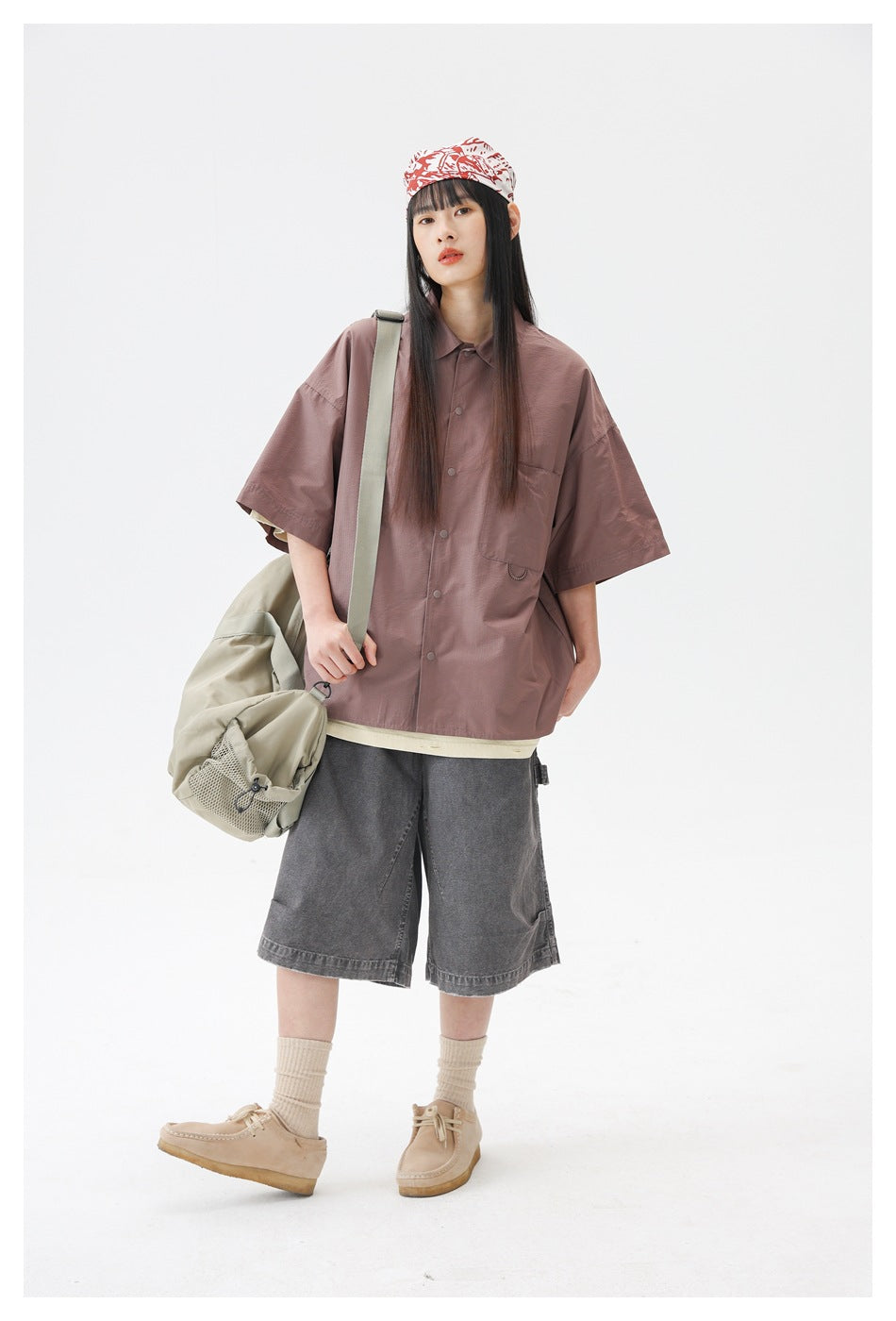 Model wearing a dusty rose oversized button-up shirt with short sleeves and a chest pocket, carrying a light khaki bag.