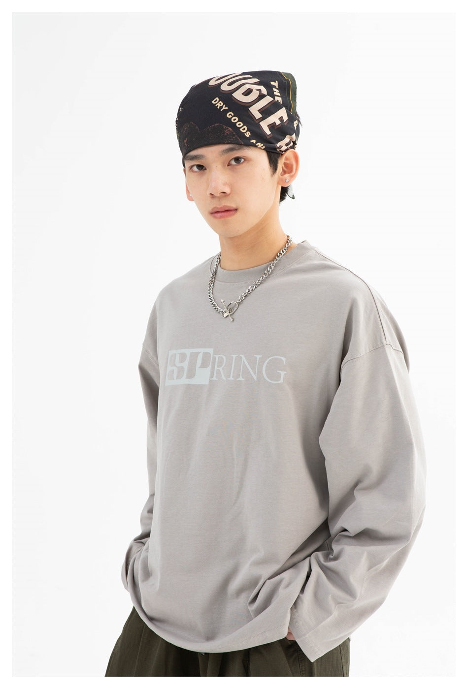 Close view of a model wearing a gray oversized long-sleeve shirt with pale SPRING lettering.
