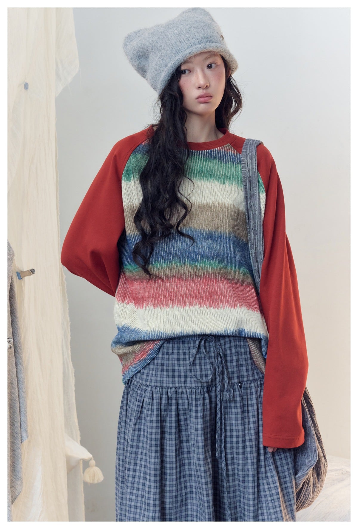 Closer view of a model in a cream multicolor striped sweater with red sleeves and a blue plaid skirt.