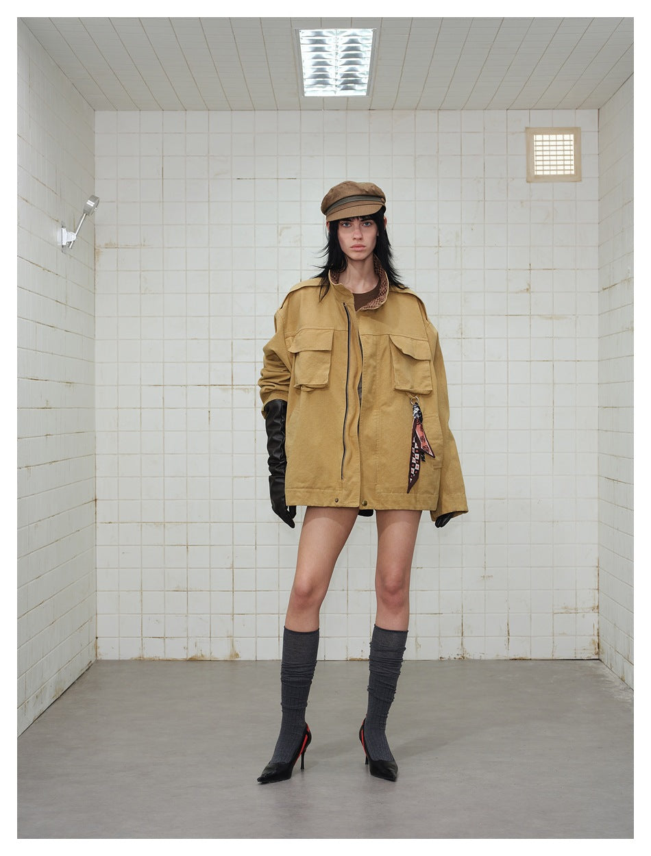 Model wearing an oversized ochre zip-front jacket with flap chest pockets, black gloves, a brown cap, and knee-high socks.