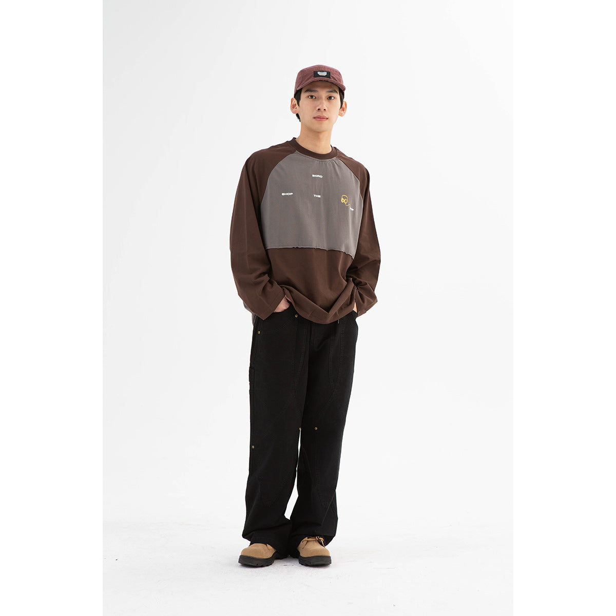 Front view of a model wearing a brown and gray color-block raglan sweatshirt with small chest graphics and black trousers.