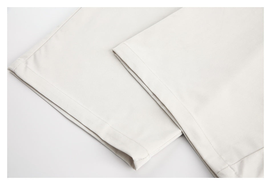 Close-up of the stitched hems on light ivory trouser legs laid flat.