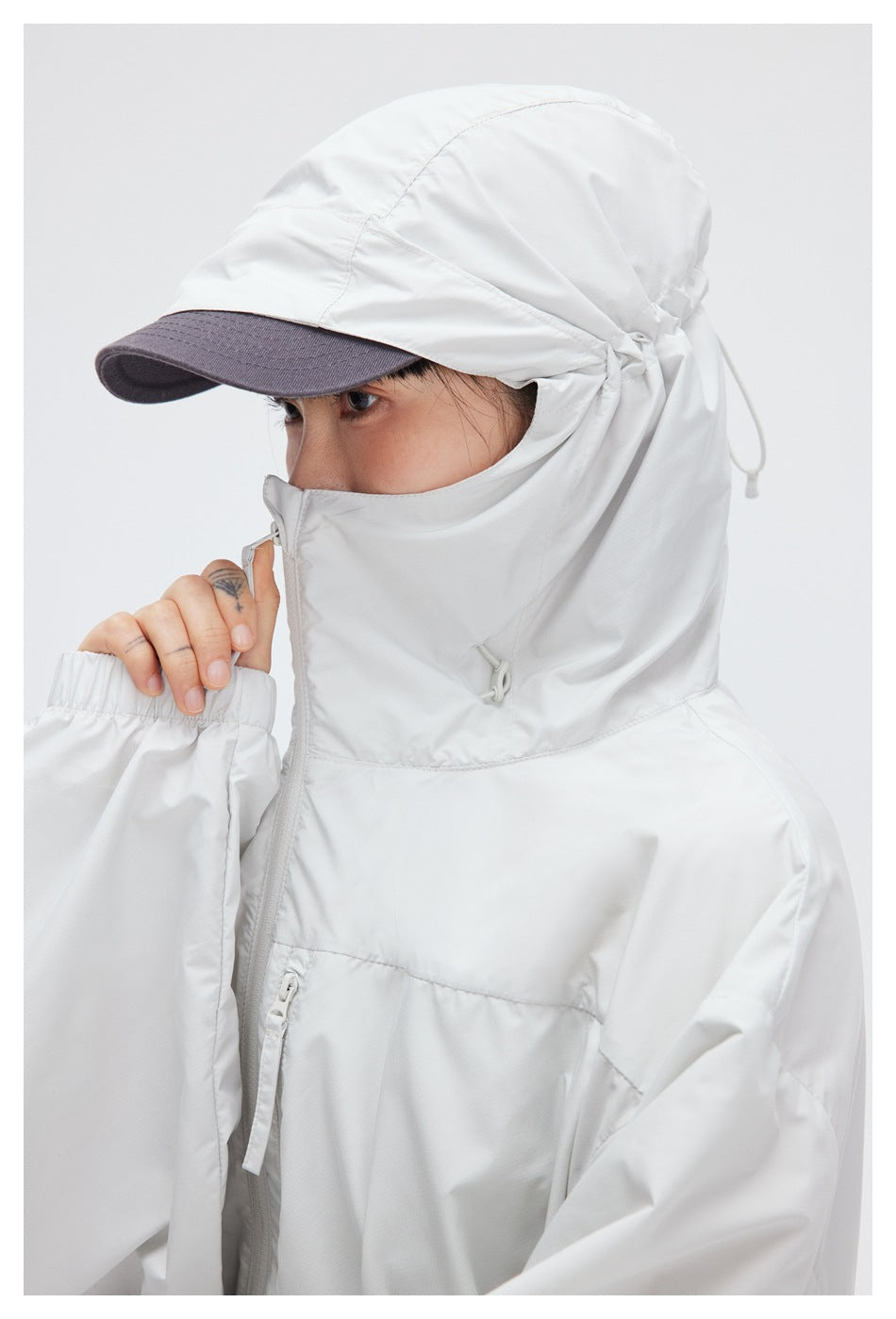 Close-up of a white jacket's hood, high collar, drawcords, front zipper, and chest pocket.
