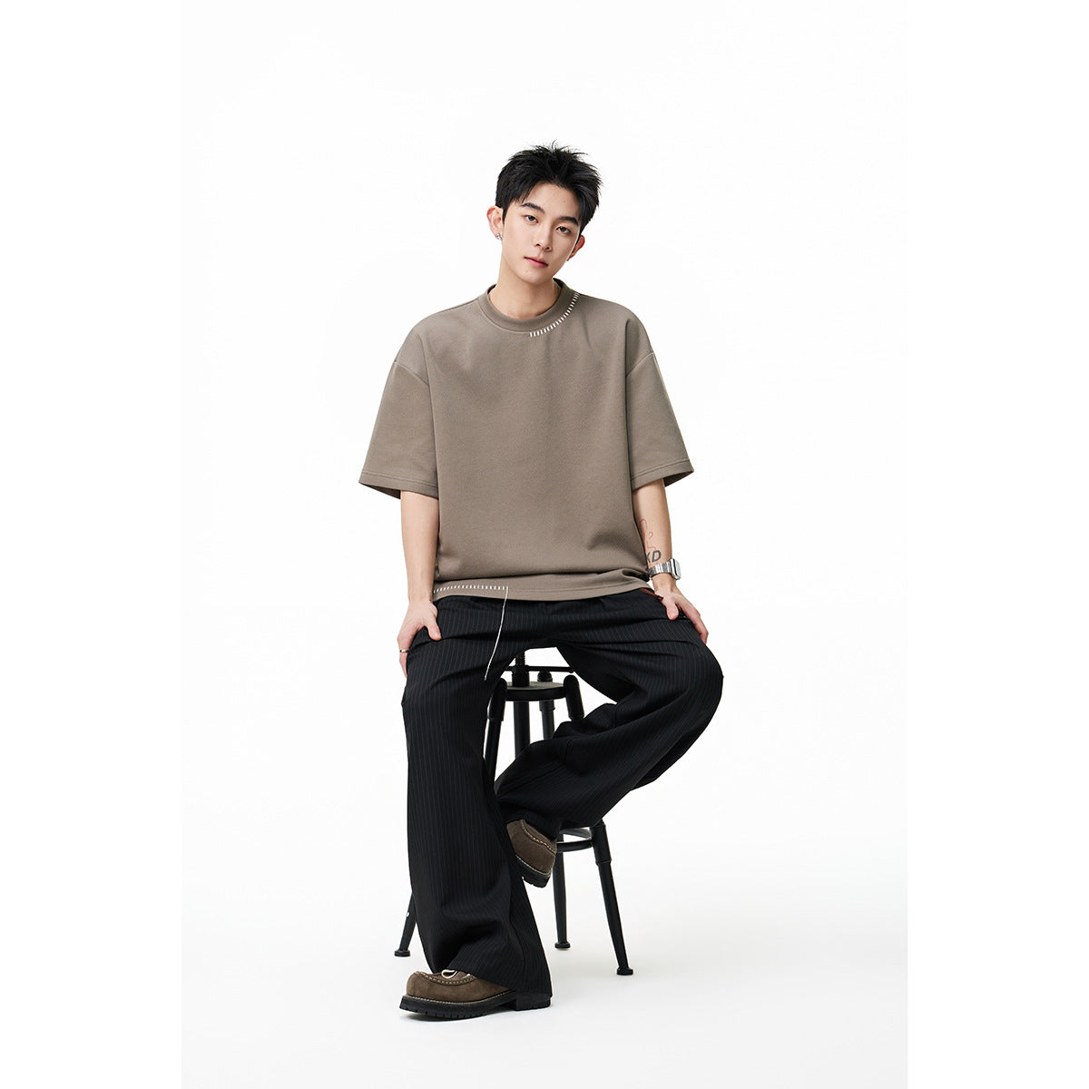 Model seated in a taupe oversized short-sleeve T-shirt with black pinstriped wide-leg pants.