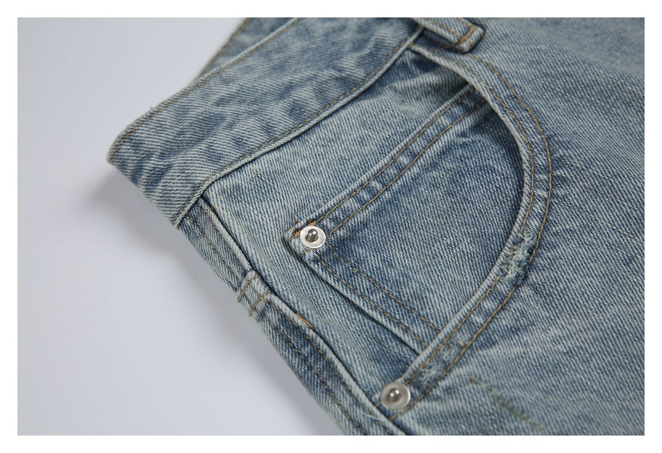 Close-up of a curved front pocket with metal rivets on light blue washed jeans.