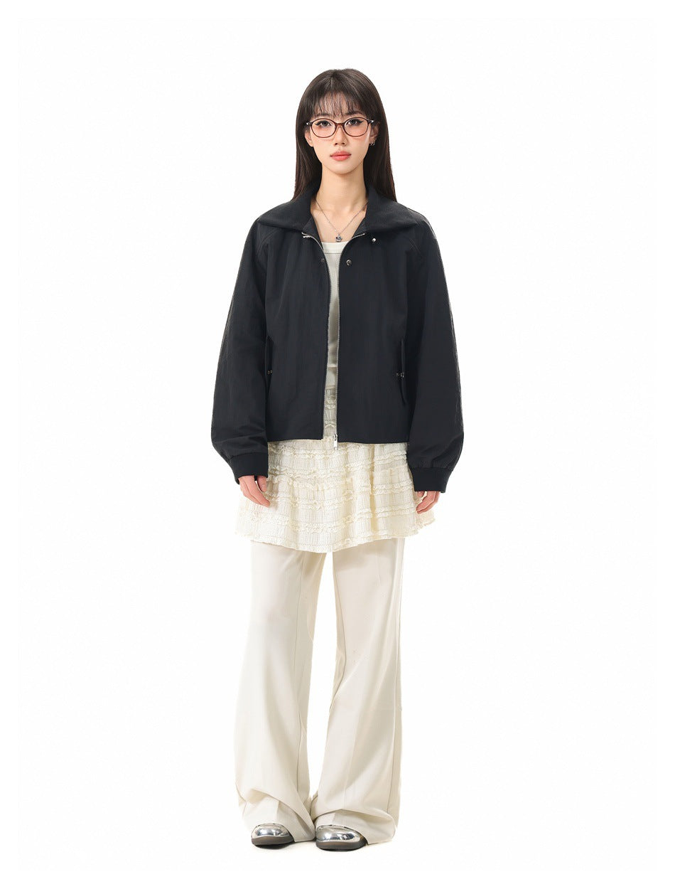 Full-length model wearing a black collared zip jacket over a cream lace top and wide-leg trousers.