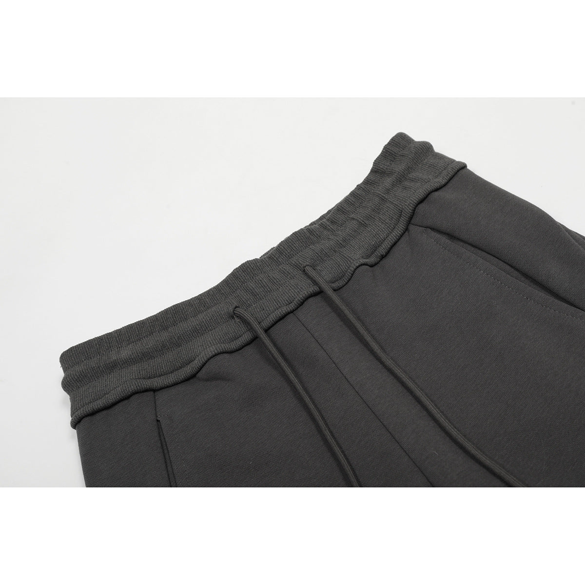 Close-up of charcoal pants showing the ribbed elastic waistband, drawstrings, and front pocket seam.