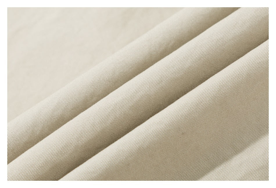 Close-up of light beige fabric folded into soft diagonal ridges, showing a fine diagonal weave.