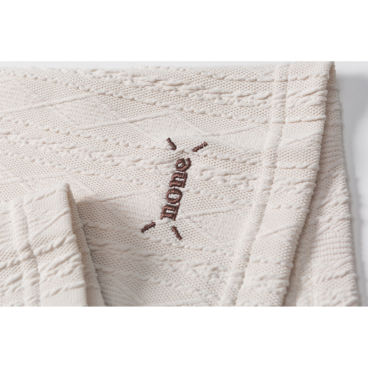 Close-up of brown embroidered lettering on the textured cream polo fabric.