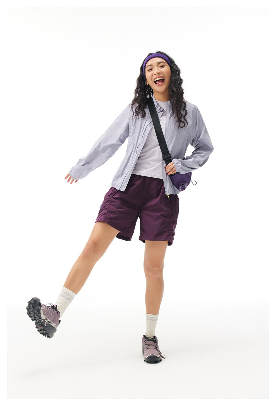Model posing in an open light lavender jacket, white top and plum shorts, with one leg extended.