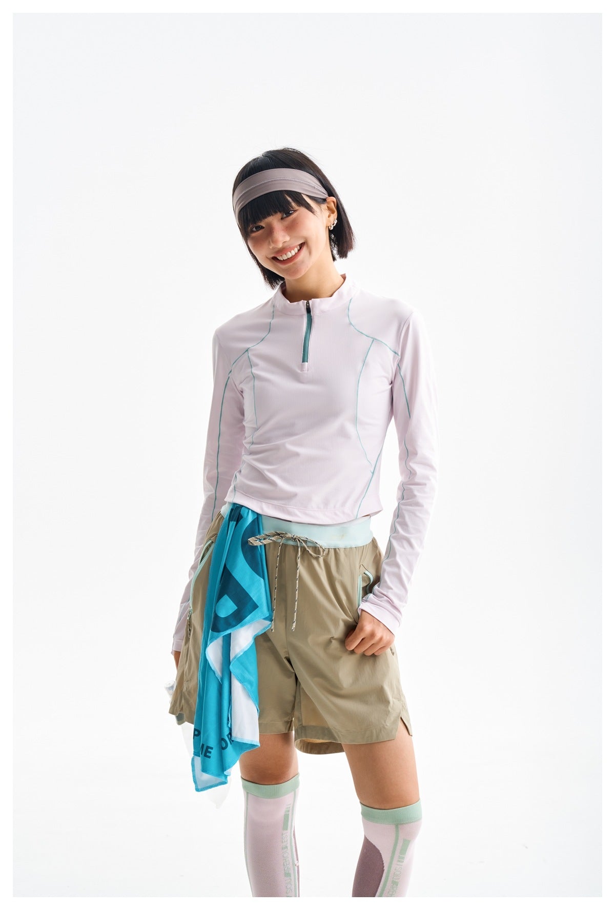 Closer view of a model in a pale pink quarter-zip top with teal seam details and tan drawstring shorts.