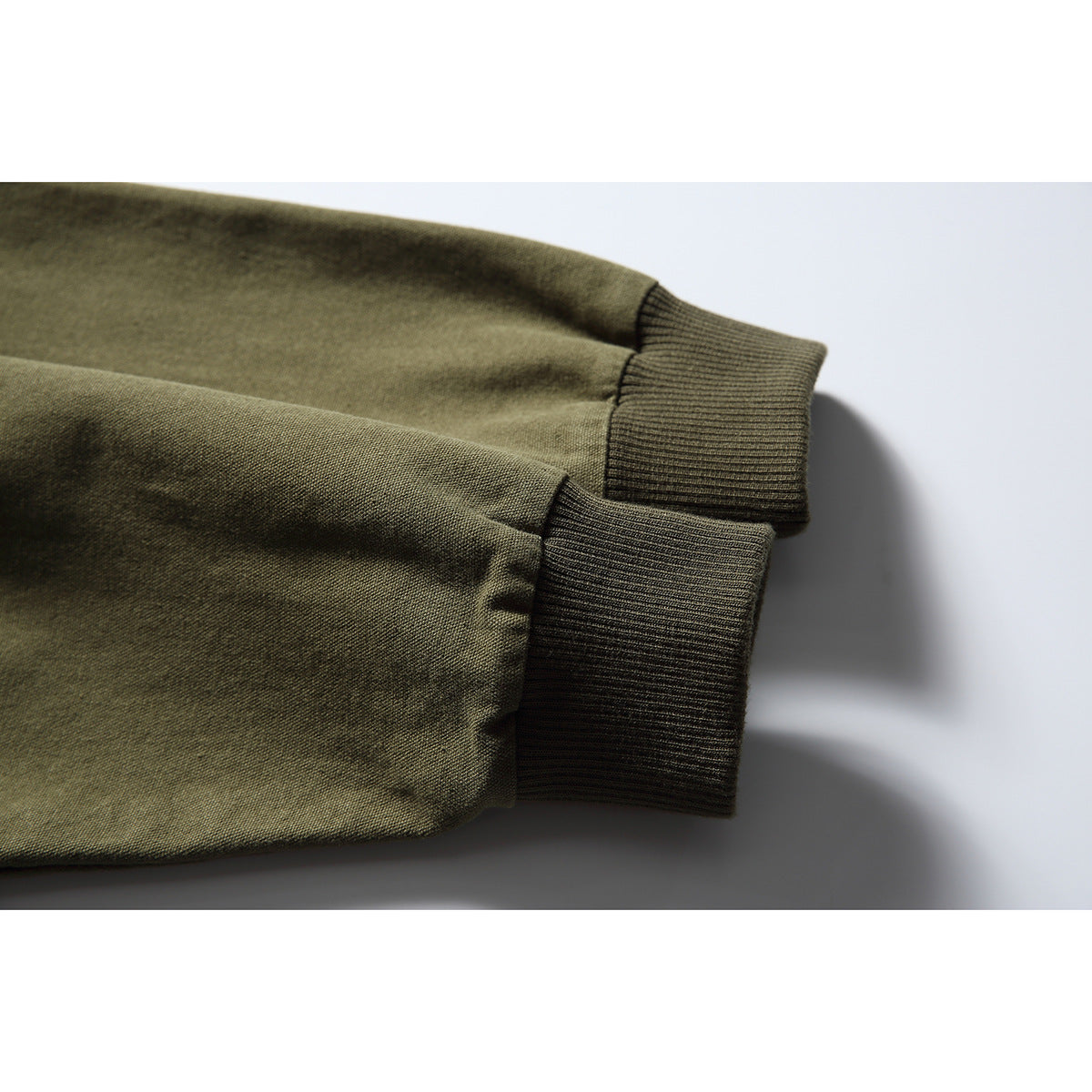 Close-up of olive jacket sleeves ending in dark rib-knit cuffs.