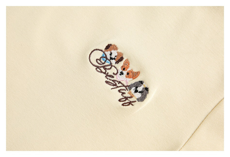 Close-up of a small embroidered group of cartoon cats and cursive lettering on cream fabric.