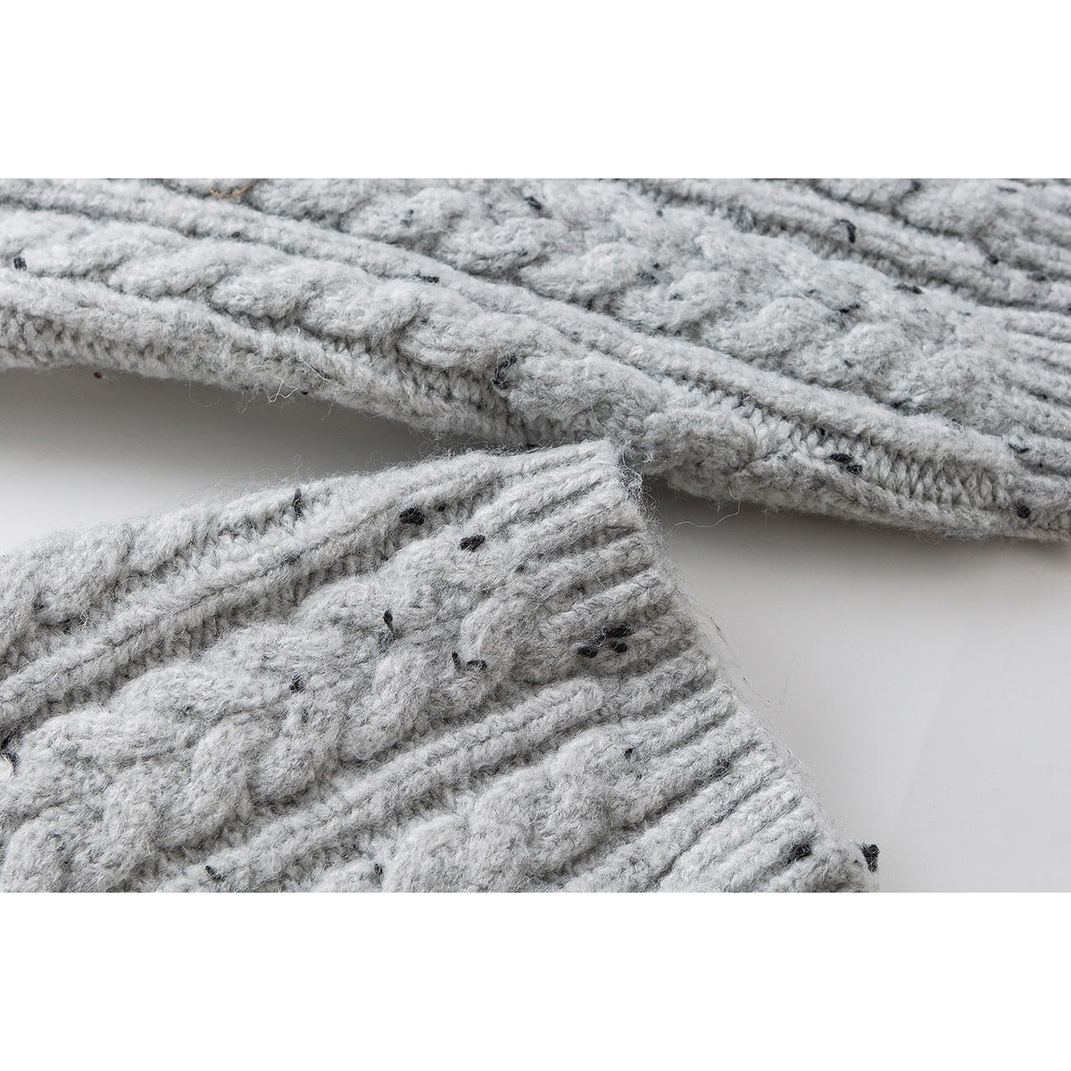 Close-up of the edge and seam of a light gray flecked cable-knit sweater.