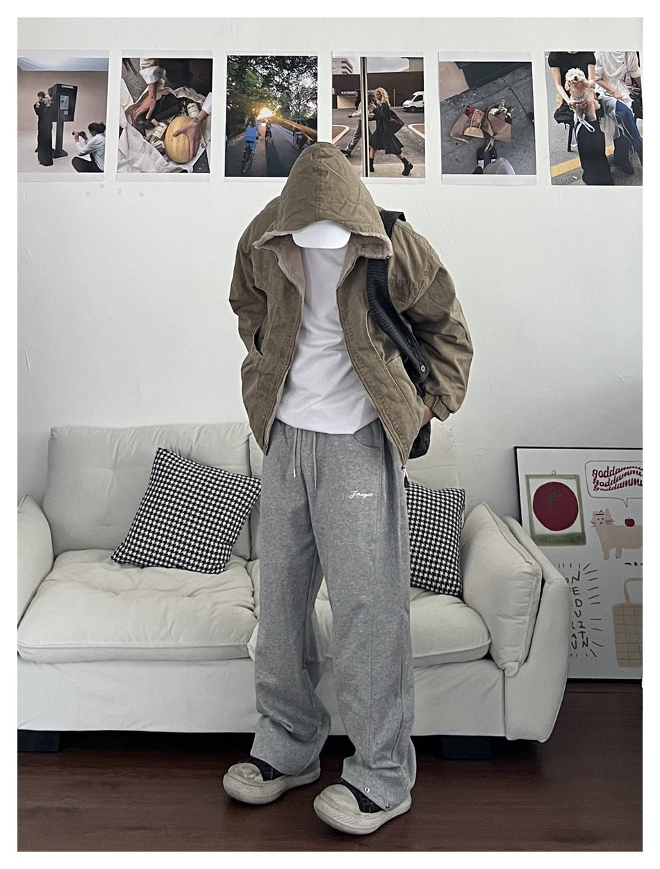 Person wearing khaki jacket with hood up over the head, open front over white tee and gray sweatpants