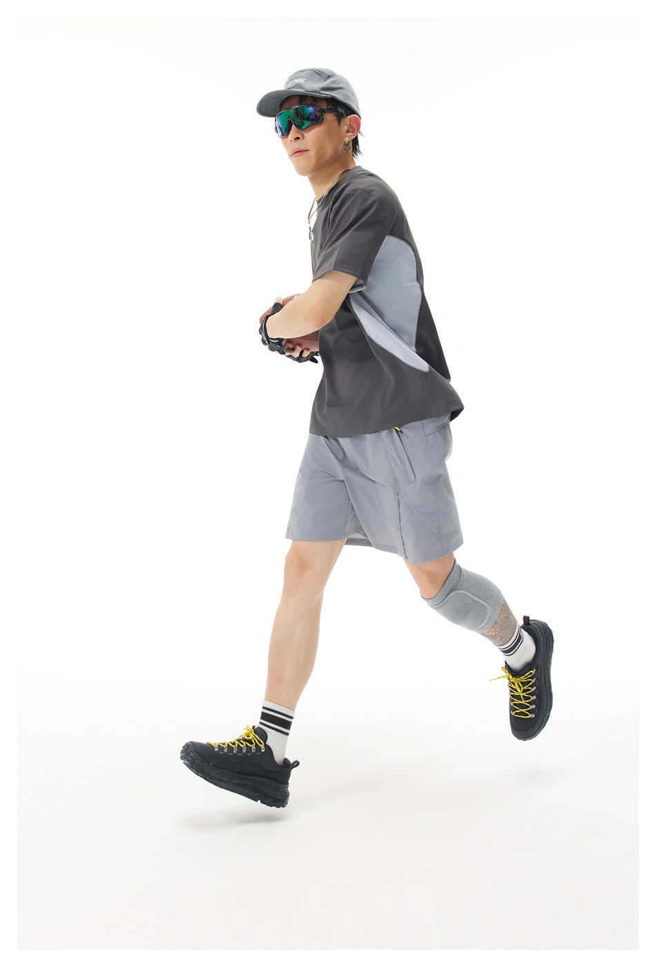 Model in a charcoal shirt with light gray side panels and matching shorts runs while holding a football.