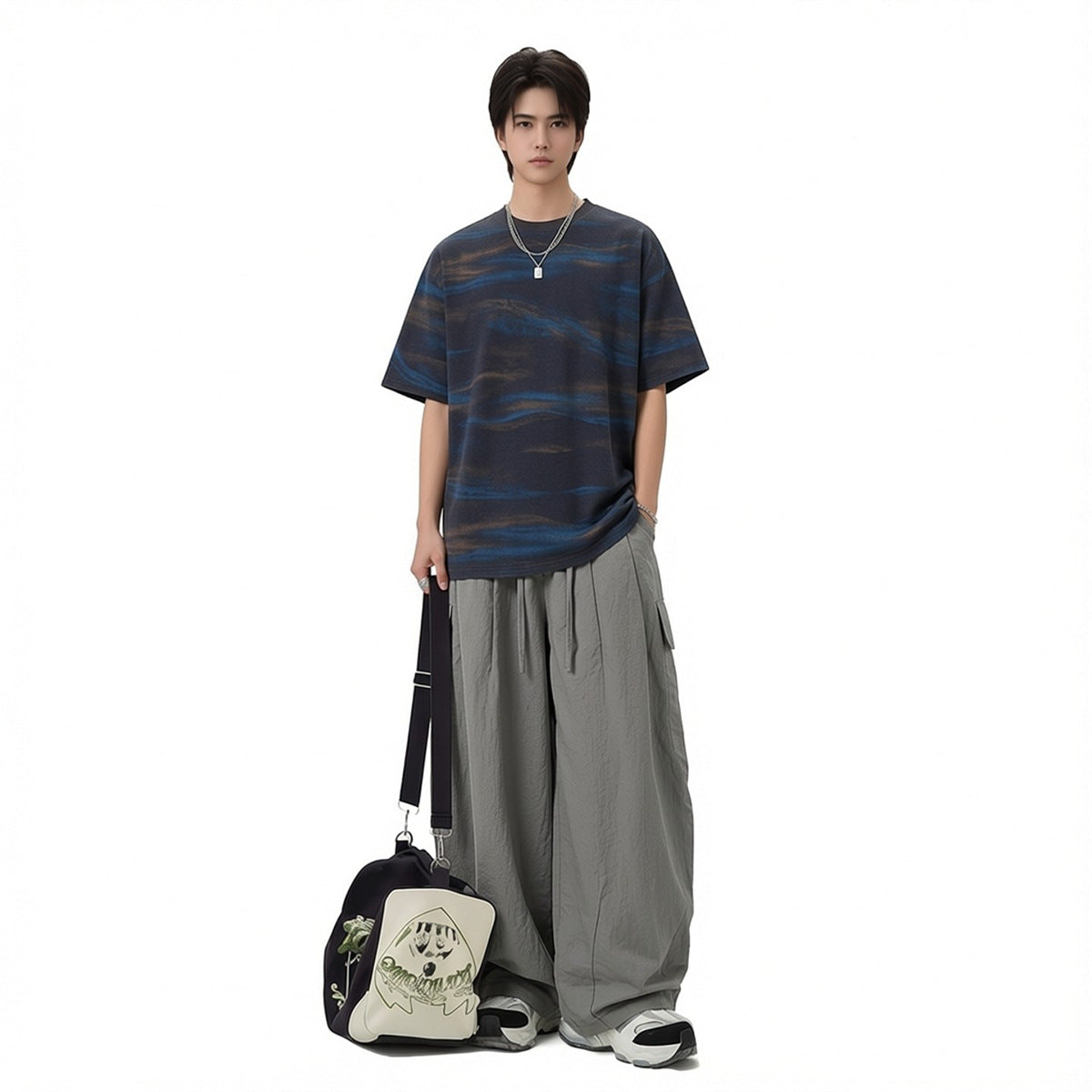 Model wearing a loose navy T-shirt with blue and brown wave stripes and wide gray cargo pants.