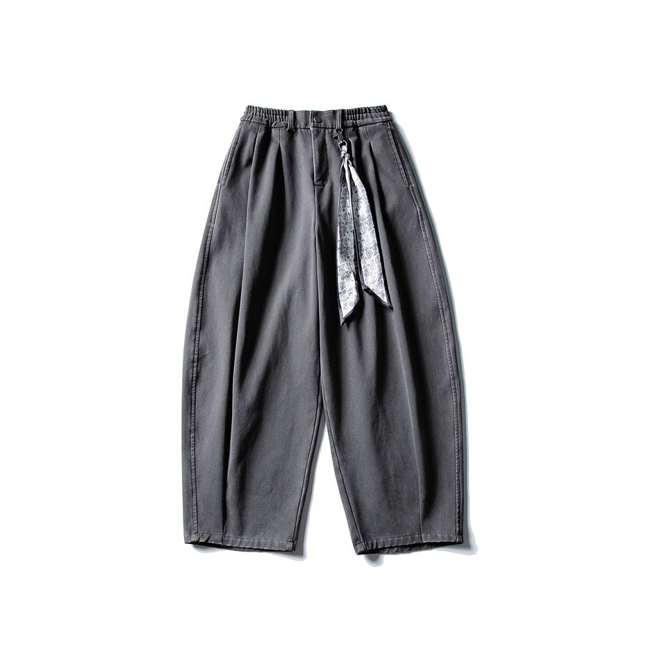 Gray wide-leg pleated pants with elastic waistband and a patterned scarf clipped at the waist, flat lay