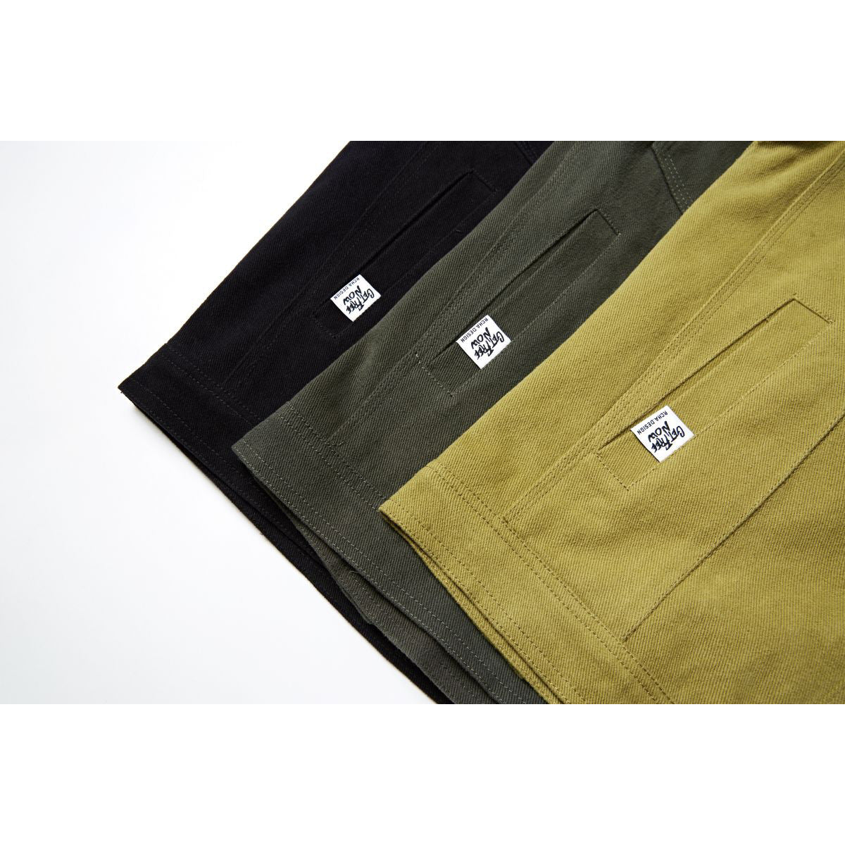 Close-up of three jackets in black, dark olive, and mustard, showing back pockets and small sewn-in labels.