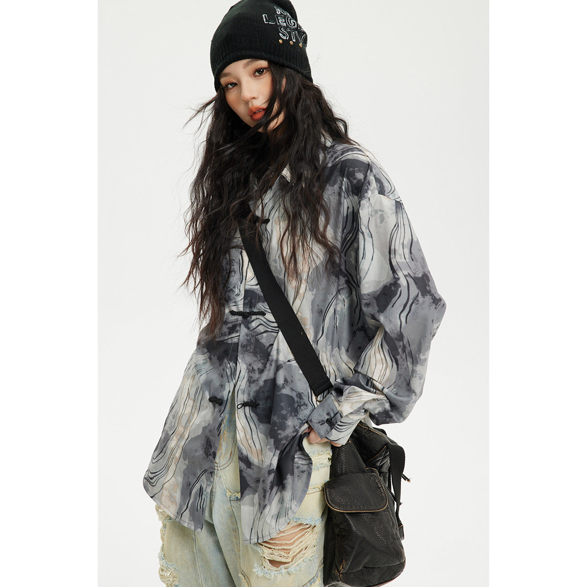 Model wearing a gray, black, and cream abstract-print shirt with frog closures, a beanie, and a crossbody bag.