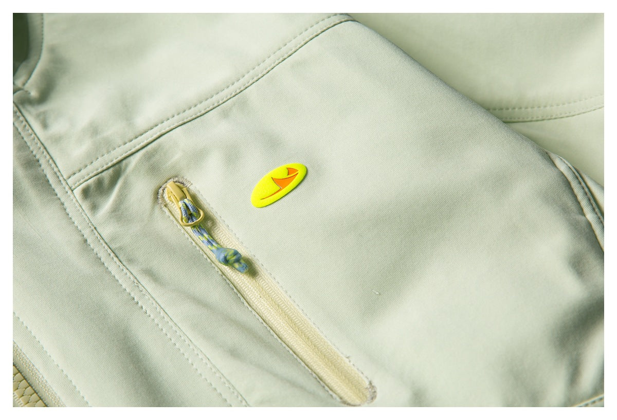 Close-up of a pale sage-green jacket chest with a narrow zipper pocket and bright yellow oval patch.