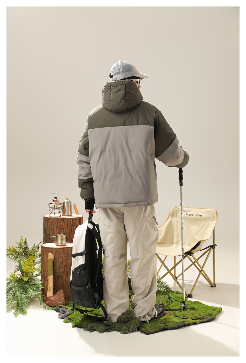 Rear view of a model wearing an olive and gray color-block hooded puffer jacket with light beige cargo pants.