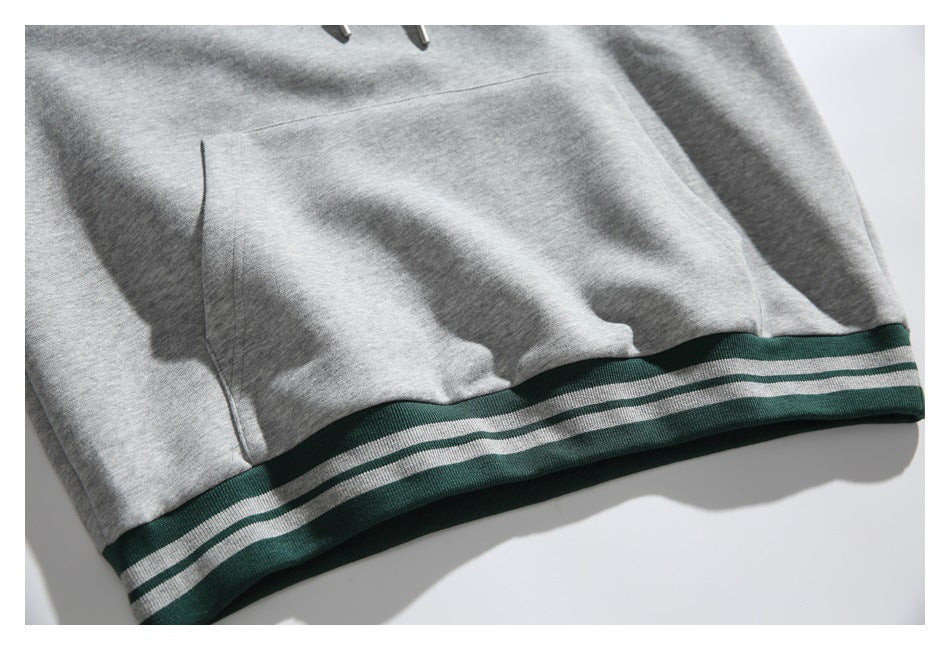Close-up of the gray hoodie’s kangaroo pocket and dark green striped ribbed hem.
