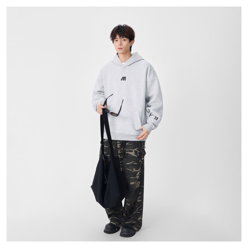 Model wearing a light gray oversized hoodie with black chest and sleeve details, styled with camouflage trousers.