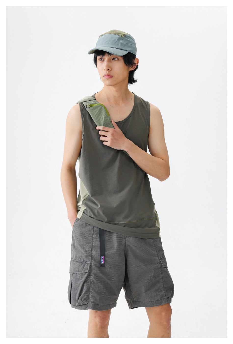 Closer view of a model wearing a gray-olive sleeveless tank with pale side panels and a green crossbody strap.