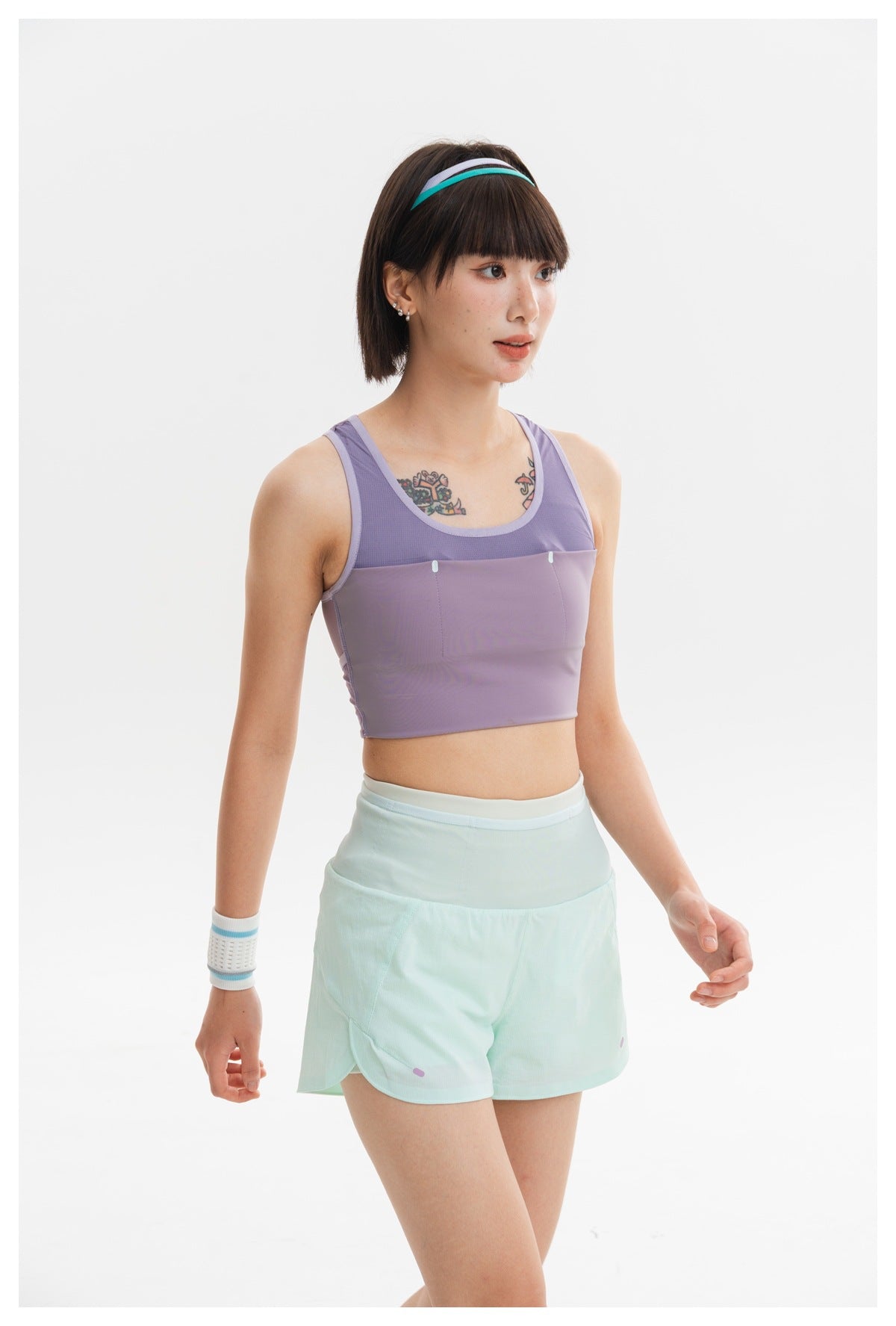 Model wearing a lavender cropped athletic tank with mesh panels and pale mint shorts, shown from a three-quarter angle.