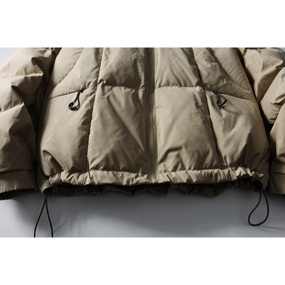 Close-up of the taupe puffer jacket's front zipper, quilted panels, and drawcord toggles at the hem.