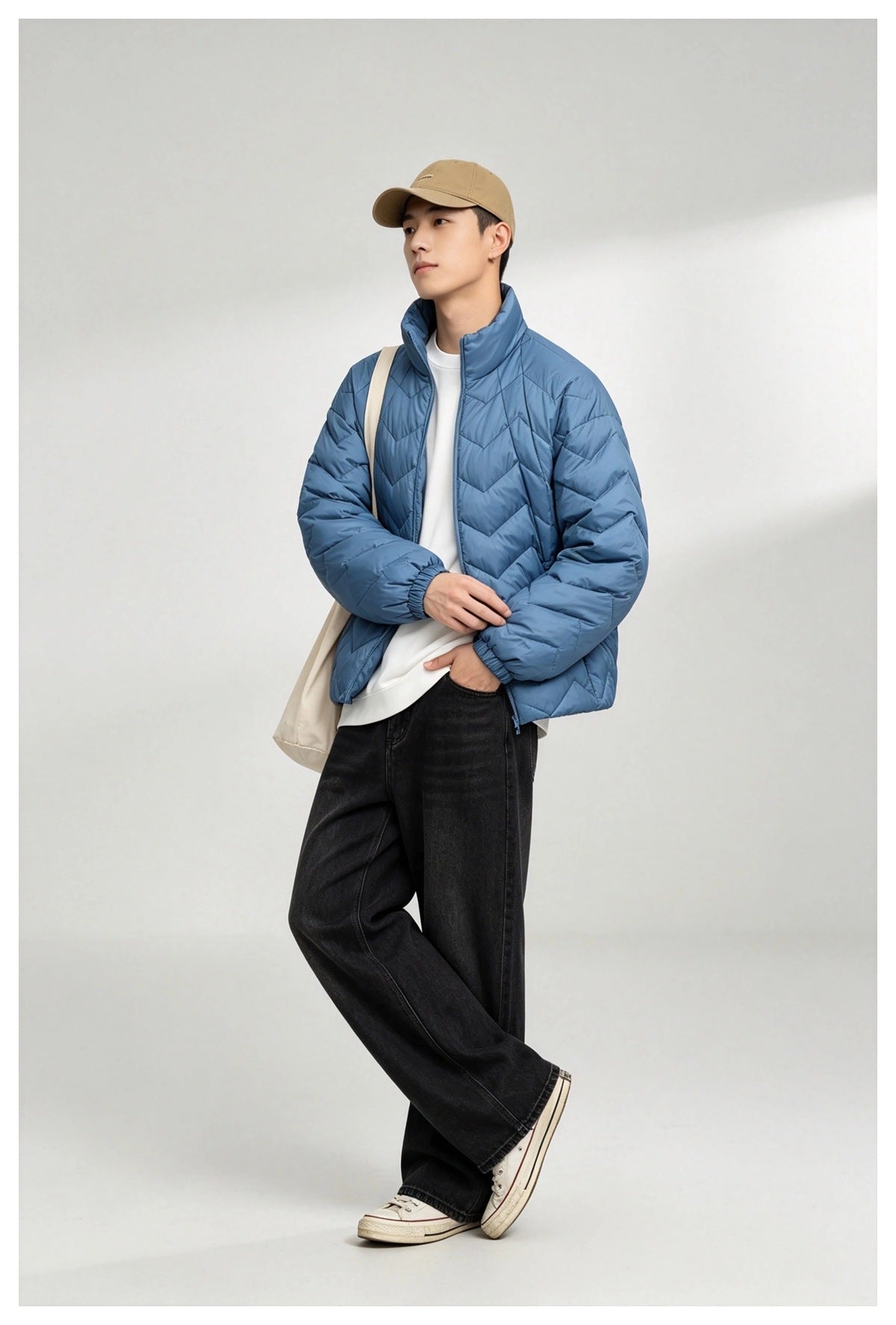 Model wearing blue quilted stand-collar jacket over a white tee, black wide-leg jeans, tan cap and canvas tote